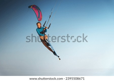 Caucasian woman kitesurfer athlete doing a trick in the air against a blue sky without a cloud. Professional kitesurfing training Royalty-Free Stock Photo #2395508671