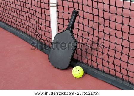 A Pickleball paddle and ball at net on pickleball court.