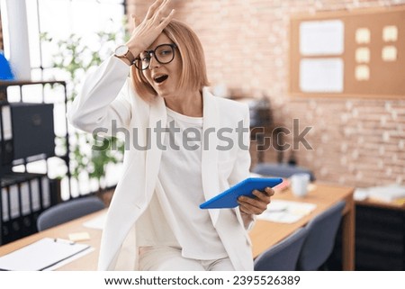 Young caucasian woman working at the office wearing glasses surprised with hand on head for mistake, remember error. forgot, bad memory concept.  Royalty-Free Stock Photo #2395526389