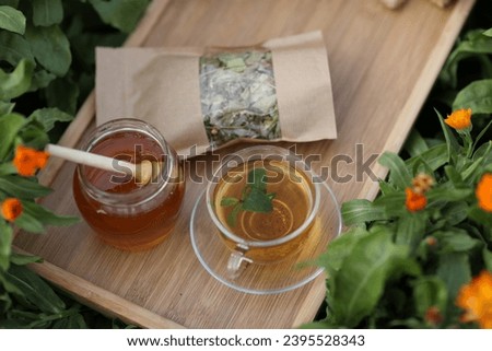 Still life of tea with mint and honey on a tray on a background of calendula flowers in the garden Pack of herbal tea Mint leaves in a mug Natural products Healthy drinks