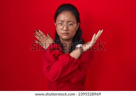 Asian young woman standing over red background rejection expression crossing arms doing negative sign, angry face 