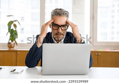 Thoughtful mature senior 50s 60s wearing eyeglasses staring at the laptop screen, holding head with both hands, concentrated experienced manager solving difficult tasks, planning business strategy