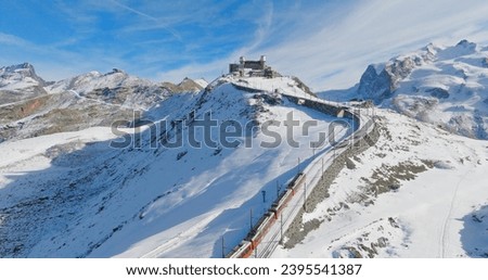 Panoramic landscape of Gornergrat bahn railway climibing up the summit station with Matterhorn mountain peak background in Zermatt on a sunny winter day. Swiss Alps, Switzerland travel journey trip.