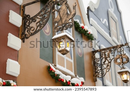 A fake wall of a building at a Christmas market. Street decorations in the style of small English houses. Panel bracket cantilever side sign in the form of a metal teapot and antique lantern



