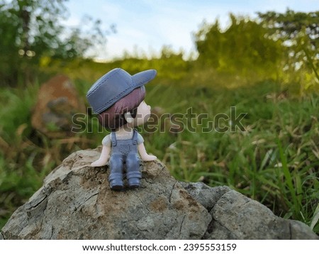Mini figure of man sitting alone on a large rock looking up at the sky with bokeh background 