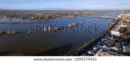 River IJssel twice its size during high water levels in winter rains seen from above passing countenance boulevard of Zutphen, The Netherlands. Aerial of flooded floodplains at city limits. Royalty-Free Stock Photo #2395579433
