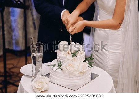 Bride and groom cut a wedding cake with a knife on a table. Cropped. Faceless Royalty-Free Stock Photo #2395601833