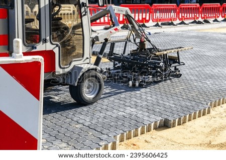 Paving block laying machine on new pavement, red temporary portable plastic safety barriers, warning sign, repaved place, street reconstruction view