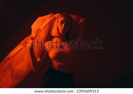 A trendsetting woman lifts her blazer above her head, creating a fashionable silhouette against a crimson-lit background