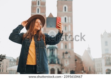 Young woman tourist in hat making selfie photo in front of the famous St. Mary's Basilica on the Market square in Krakow, Poland. Traveling Europe in autumn. Vacation concept