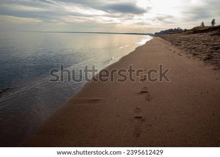 Footsteps in the sand along Lake Superior shoreline in autumn.  Colorful sunrise reflected on calm water with tan sand shoreline.
