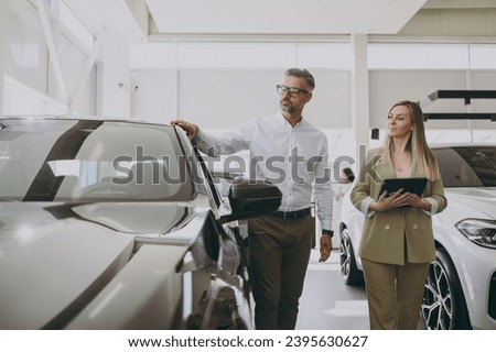 Adult man customer male buyer client wears shirt consult with salesman hold documents choosing auto want to buy new automobile in car showroom vehicle salon dealership store motor show. Sales concept Royalty-Free Stock Photo #2395630627