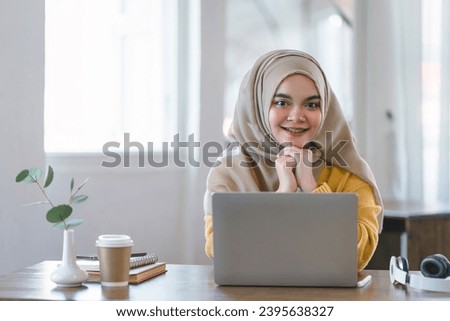 A happy teenage Muslim girl looking at the camera while relaxing during a break in her online class at home