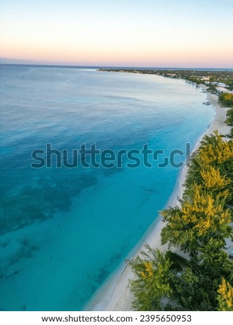 Aerial of Golden Sunrise at Seven Mile Beach, Grand Cayman, Cayman Islands a tropical destination within the Caribbean with a Relaxing View of Beachfront Condos, Hotels, and Lush Greenery