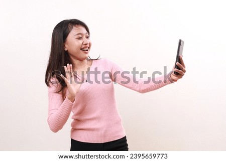Cheerful young asian girl standing while doing video call on her phone. Isolated on white background