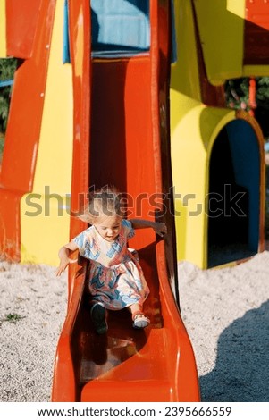 Little girl with flying hair slides down a slide holding onto a handrail Royalty-Free Stock Photo #2395666559