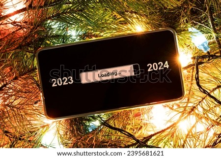 the concept of changing the year from 2023 to 2024. smartphone on the decorated fir branches in bright lights of garlands with the process of loading the new year. end of 2023