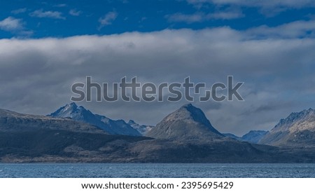 The beautiful Andean Martial mountain range  against a background of blue sky and clouds. Green vegetation, patches of snow on the slopes.  View from the Beagle Canal.