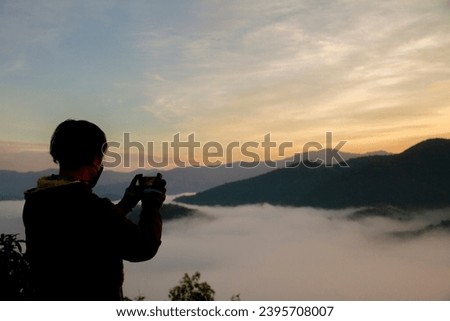 A man holds a phone and takes a photo of the sea of clouds in the morning.