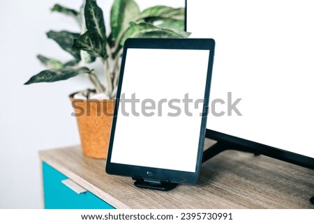 Mockup tablet stands on a wooden table near led tv with blank screen and house plant