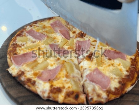 Hawaiian Pizza on wooden plate. Closeup chef cuts freshly prepared pizza slices. Hand of chef baker in white uniform cutting pizza at kitchen. Pizza picture free space for text.  
