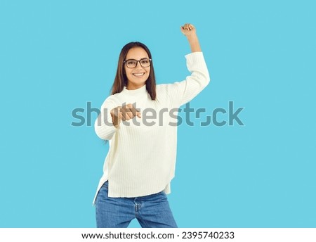 Beautiful young brunette in a white sweater and blue jeans pretends that she is riding a horse, wants to throw a lasso. Studio isolated shot on a blue background.