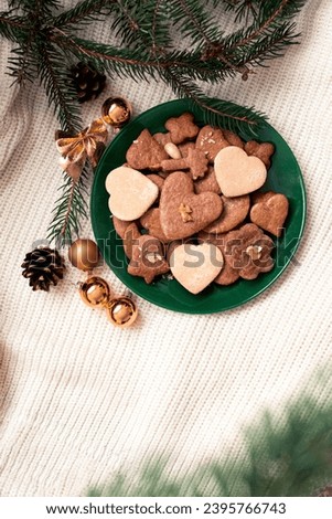 Green plate overflows with an assortment of gingerbreads and heart-shaped line cakes resting on a white wool surface. Moody tones of green, white, and brown create an ambience of warmth