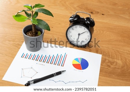 A plant, a graph, and a clock on the desk.