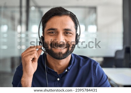 Happy Indian man call center agent wearing headset in office. Smiling male contract service representative telemarketing operator looking to camera working in customer support. Headshot portrait. Royalty-Free Stock Photo #2395784431