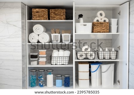 White bathroom laundry comfortable storage organizing. Rolled towels toilet paper washing powder and capsule in can and basket. Soap and washcloth arrangement on shelves eco style minimalism Royalty-Free Stock Photo #2395785035