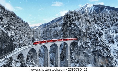 Snow falling and Train passing through famous mountain in Filisur, Switzerland. Train express in Swiss Alps snow winter scenery.  Royalty-Free Stock Photo #2395790421