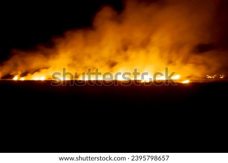 Fires are raging in dry fields and stubble in the winter and the strong winds are blurring them. Royalty-Free Stock Photo #2395798657