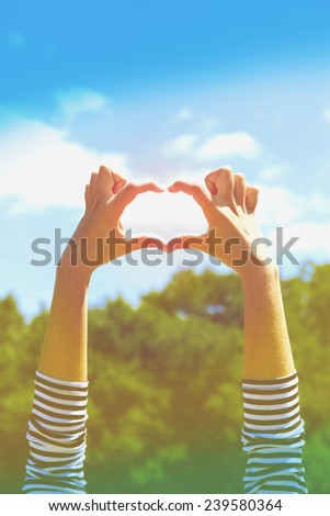 Young woman's hands making heart shape frame on blue sky background