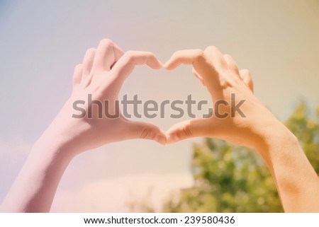 Young woman holding hands in heart shape framing on blue sky background