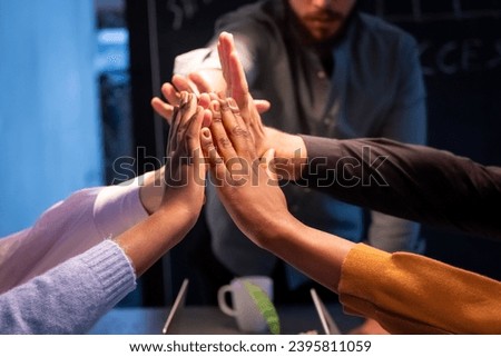 This image vividly captures the essence of teamwork and collaboration with a group of individuals partaking in a collective high five. The variety of skin tones signifies a multicultural team, and the Royalty-Free Stock Photo #2395811059