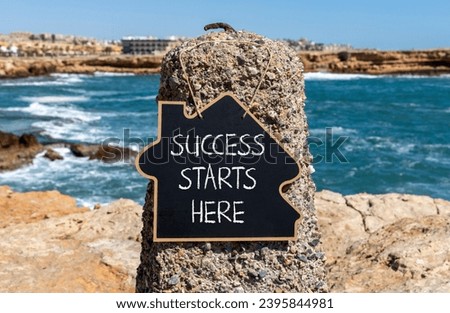 Success starts here symbol. Concept word Success starts here on beautiful black blackboard. Beautiful stone beach sea blue sky background. Business motivational success starts here concept. Copy space Royalty-Free Stock Photo #2395844981