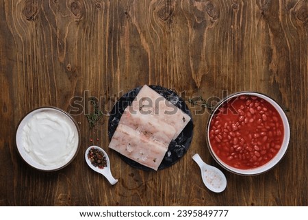 Prepared ingredients for cooking fish and beans in tomato sauce with sour cream sauce on a wooden background. Main dishes. Fish recipes.