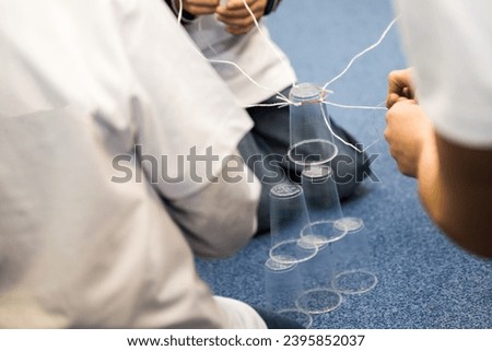 Activity aimed at coordination, cooperation of a team of children or students at school. A fun task with plastic cups, strings and rubber bands. Royalty-Free Stock Photo #2395852037