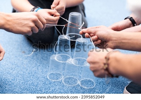 Activity aimed at coordination, cooperation of a team of children or students at school. A fun task with plastic cups, strings and rubber bands. Royalty-Free Stock Photo #2395852049