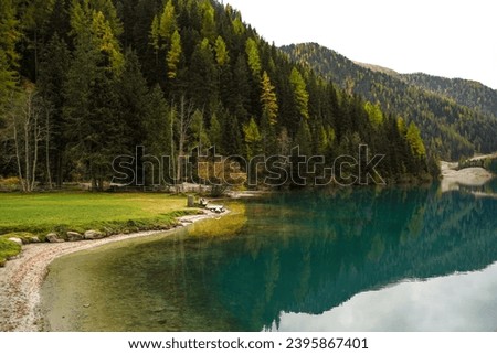 Panorama of green and yellow forest and Anterselva lake with blue calm water in Dolomites of Italy. Nature background. Beautiful wallpaper. Idyllic, harmonious atmosphere                      