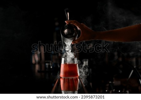 Hand of girl bartender accurate pours steaming cocktail from steel shaker into drinking glass standing on the bar counter on dark blurred background Royalty-Free Stock Photo #2395873201