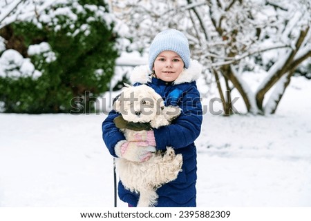Little school girl playing with little maltese puppy outdoors in winter. Happy child and family dog having fun with snow.