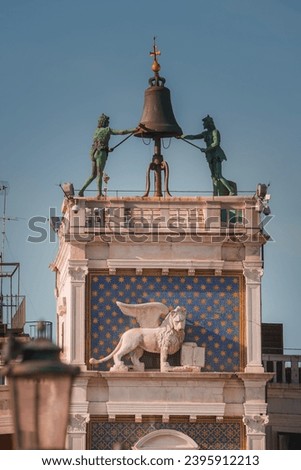 Aerial view of lion statue and bell on a building in Venice, Italy. The lion is a common symbol in Venetian culture, adding historical and architectural significance to the unique structure.