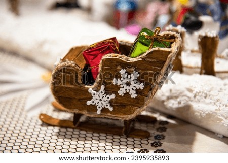 Christmas village miniature, homemade model. Made mostly of household waste materials and foam. Wooden Santa's sleigh fulfilled with gifts. Carved snowflake decor. Magic holiday atmosphere. Kids' toy 