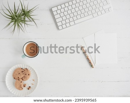 Break and snack in office work. Flat composition with copy space on white desk table with coffee cup and plate of cookies next to paper and pen next to computer keyboard.