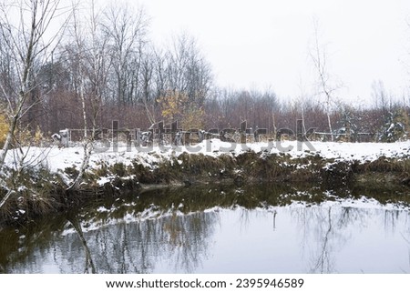 Amazing winter rural landscape with a frozen small pond. Silhouettes of trees on the river bank