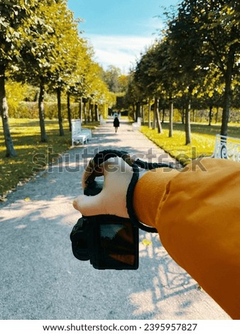 In a park, amidst trees, a man photographs a girl walking on a path, showcasing a first-person viewpoint. pov