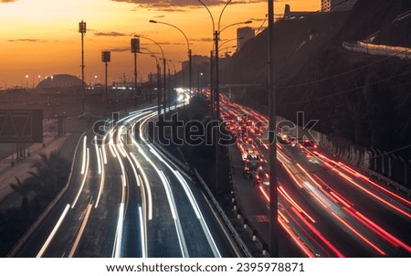 Highway at dusk with the light trails of the cars. The highway is curving to the right and has multiple lanes. The light trails are red and white, indicating the direction of the cars.