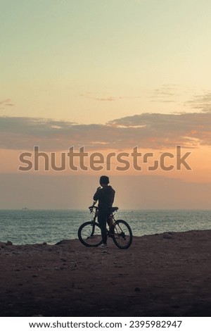 A peaceful and serene image of a person with their bike on a beach at sunset