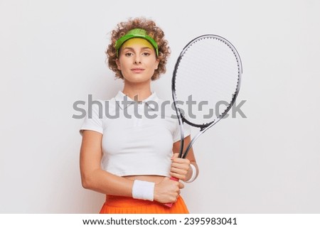 Photo of young woman posing with tennis racket in studio wearing white T-shirt and green sunshade on her head, active life concept, copy space.